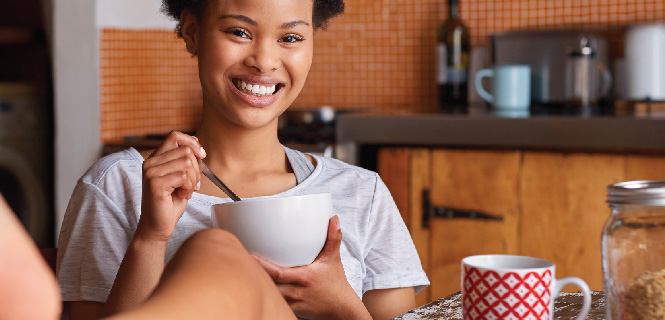 woman smiling eating a bowl of cereal at a kitchen table